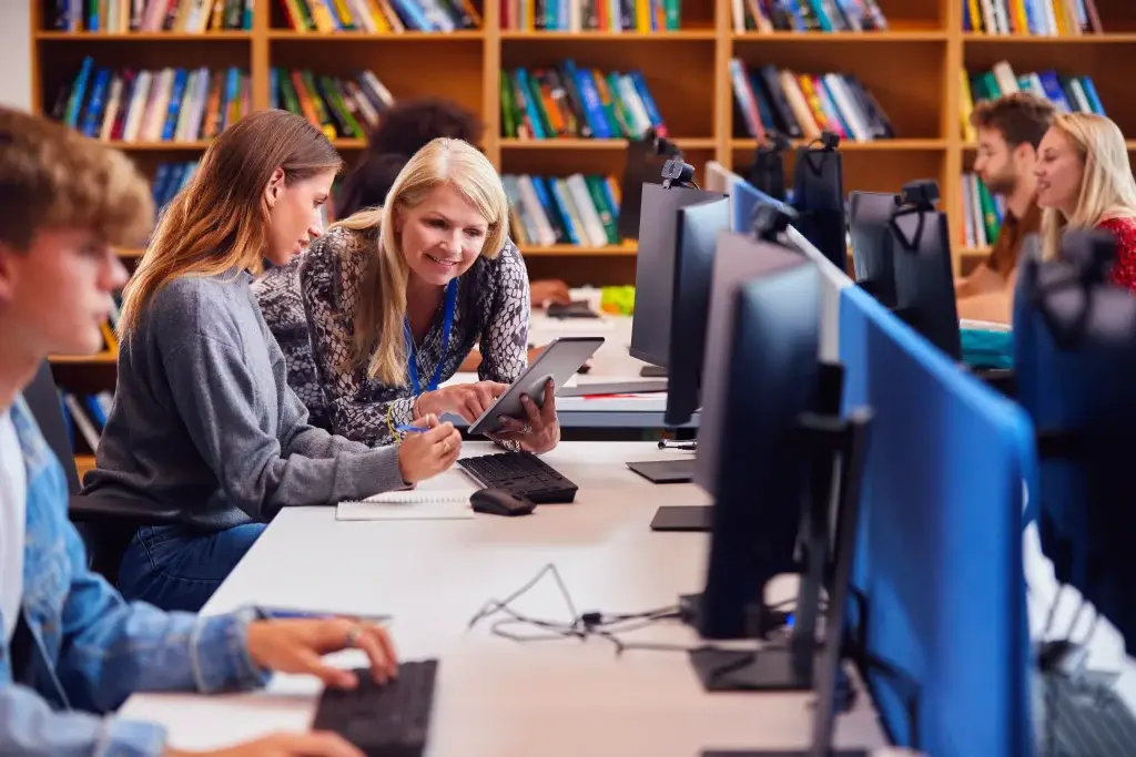 Female university student working at a computer in a library with other students.